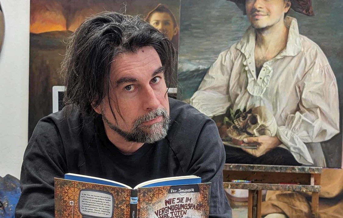 Ein Mann mit langen dunklen Haaren und grau meliertem Bart sitzt in schwarzem Pullover vor einem Gemälde. Er liest konzentriert in einem aufgeschlagenen Buch mit dem Titel "Wie sie im Vergnügungspark ihre Toten" von Veit Sprenger. Im Hintergrund ist ein klassisches Porträtgemälde zu sehen, das eine Person in einem weißen Rüschenhemd zeigt.