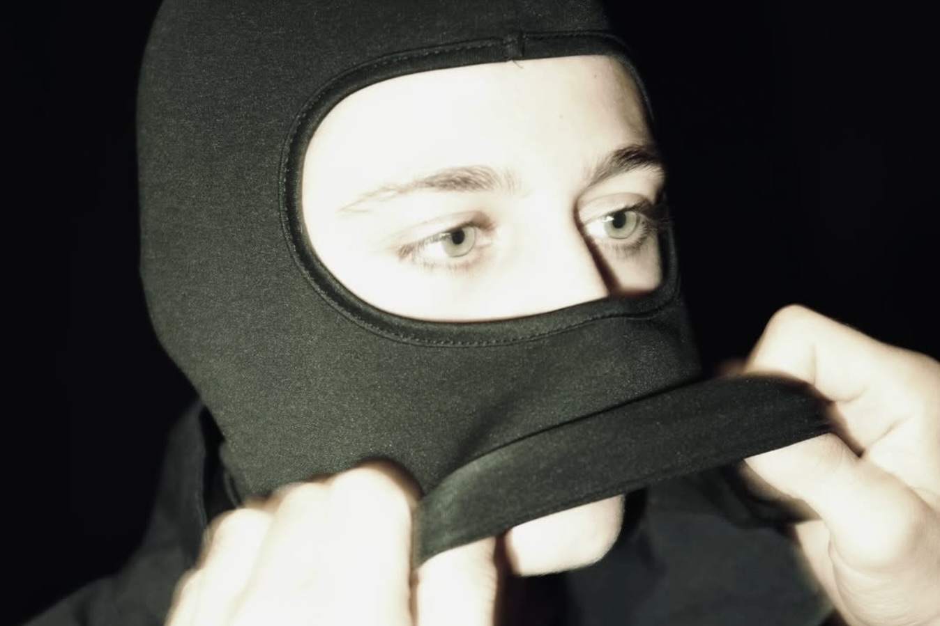 Person zieht sich eine dunkle Kapuze über den Kopf, Hände greifen den Stoff, die Szene ist stark abgedunkelt.